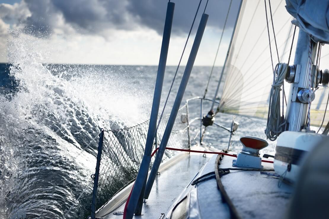 Ein Segelboot fährt auf dem Wasser an einer Welle