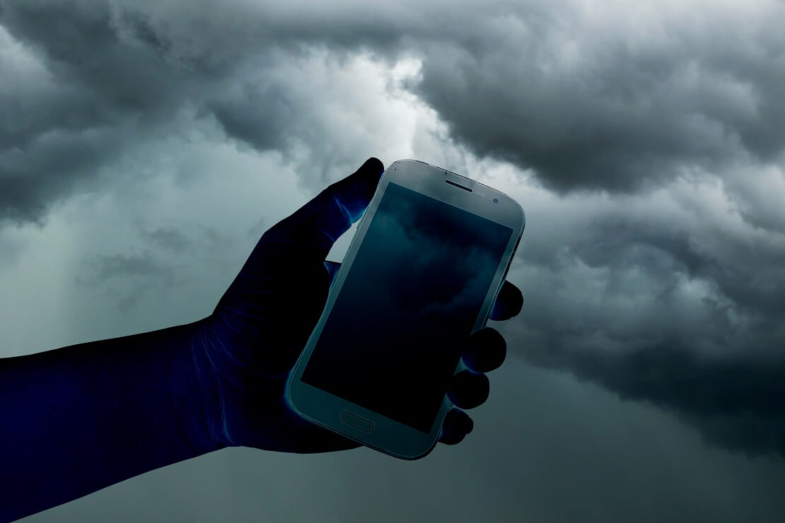 Ein Handy wird hochgehalten im Hintergrund sind dunkle Wolken zu sehen