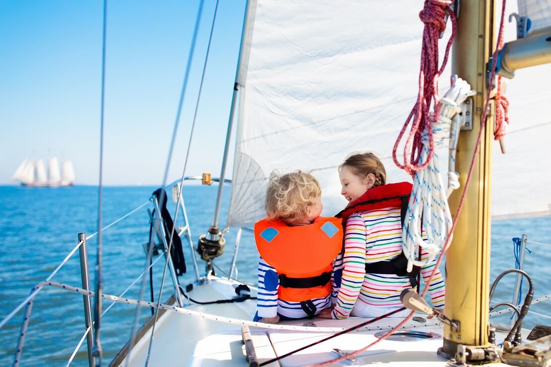 Kinder sitzen mit Rettungsweste auf einem Segelboot