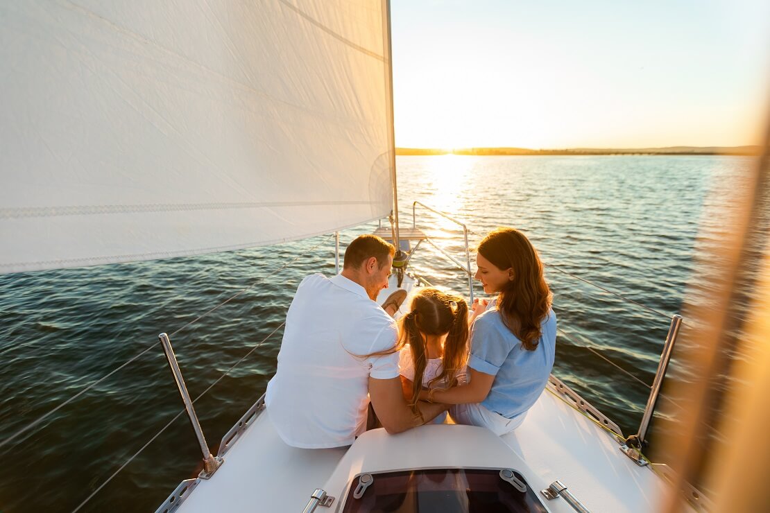 Mann und Frau mit einem Kind an Deck von einem Segelboot bei Sonnenuntergang